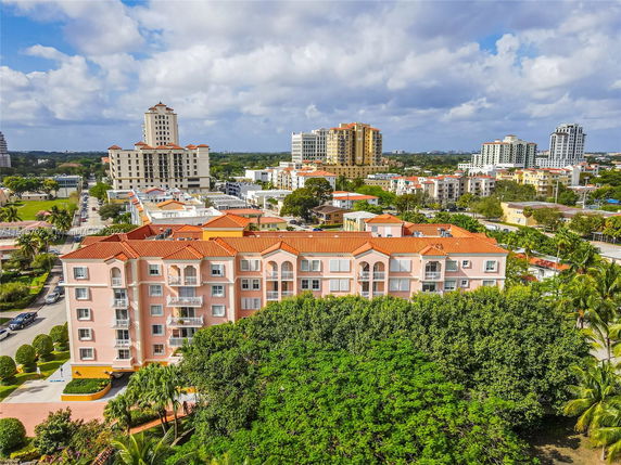 Aerial view of a multi-story building surrounded by trees and other buildings in an urban area.