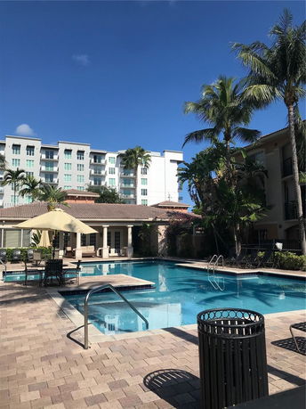 Outdoor swimming pool area with nearby buildings and palm trees.