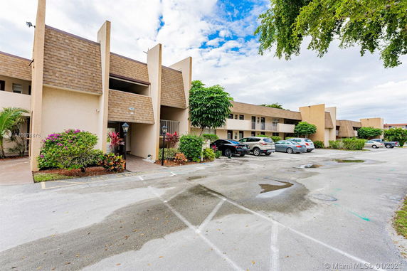 Front view of a multi-story building with parking spaces and trees.