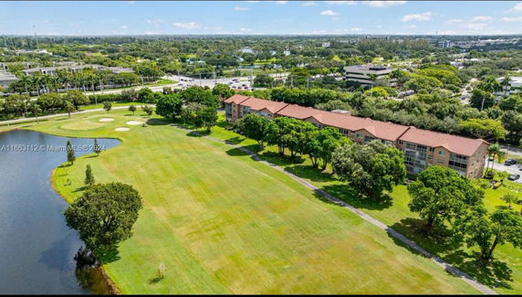 Aerial view of a landscape with buildings, grassy area, trees, and a body of water.