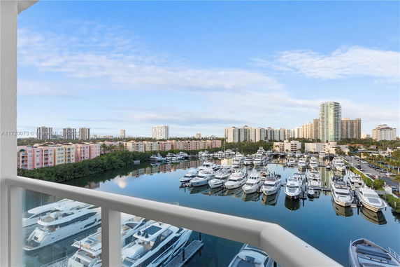View from a balcony overlooking a marina with yachts and distant high-rise buildings.