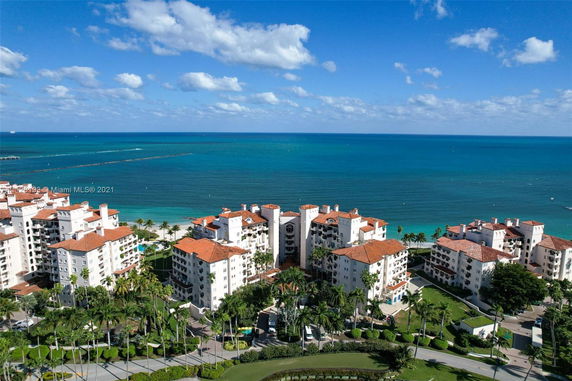 Aerial view of several multi-story buildings with red-tiled roofs on a coastline next to a blue ocean.