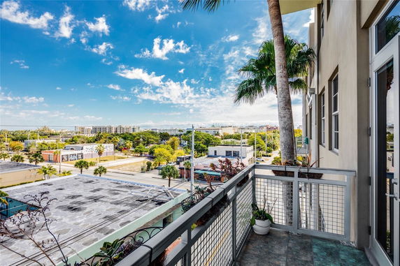 View from a balcony overlooking a cityscape with palm trees and various buildings in the distance.