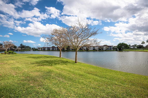 View of a lake with apartment buildings in the background and trees in the foreground.