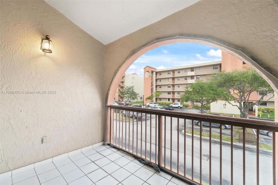 View from a balcony overlooking a multi-story residential building and parking lot.