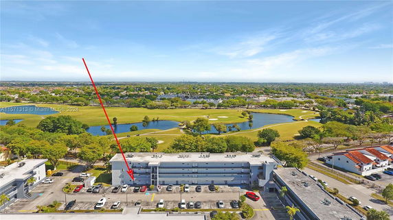 Aerial view of an apartment building with a parking area, overlooking a golf course and surrounding landscape.