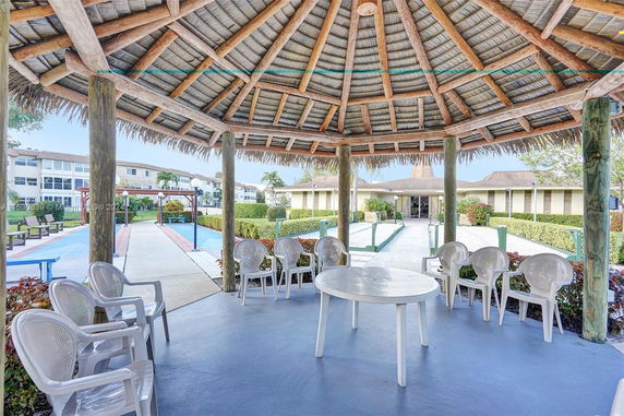Outdoor space with a seating area under a thatched roof and a view of pathways and benches.