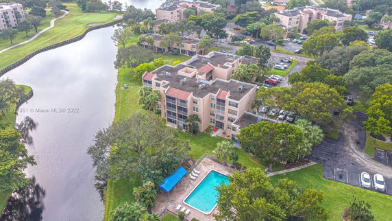 Aerial view of a building with a swimming pool, parking area, and a nearby waterway.