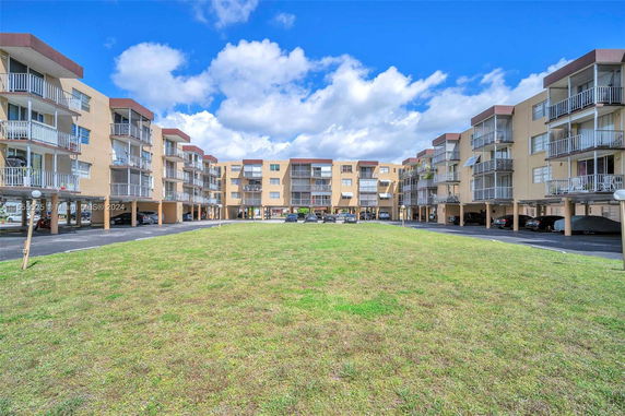 Front view of a multi-story apartment complex with balconies and parking areas.