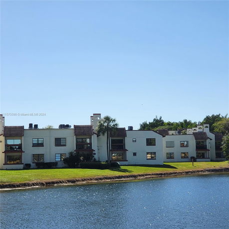 View of a multi-story building with white walls and brown roof tiles next to a body of water.