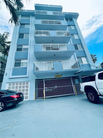 Front view of a multi-story apartment building with balconies and a parking area below.