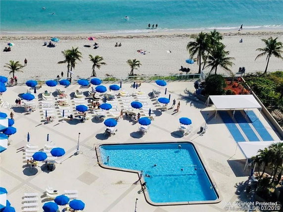 View of a beachside area with a pool, blue umbrellas, and sun loungers.