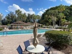 Outdoor swimming pool area with surrounding lounge chairs and tables with umbrellas.