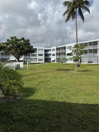 Front view of a multi-story building with balconies and surrounded by a grassy area.