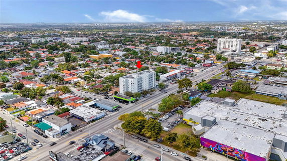 Aerial panoramic view of an urban area with residential buildings and a prominent multi-story building marked by a red arrow.