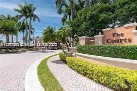 Entrance view with palm trees, green hedges, and a sign for 'The Courts'.