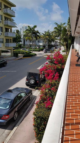 View overlooking a street with cars parked alongside, palm trees, and nearby buildings.