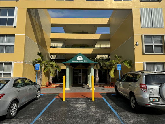 Front view of a multi-story building with yellow exterior and parking spaces in front.