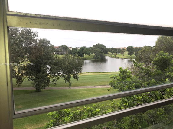 View from a window overlooking a golf course with trees and a pond.