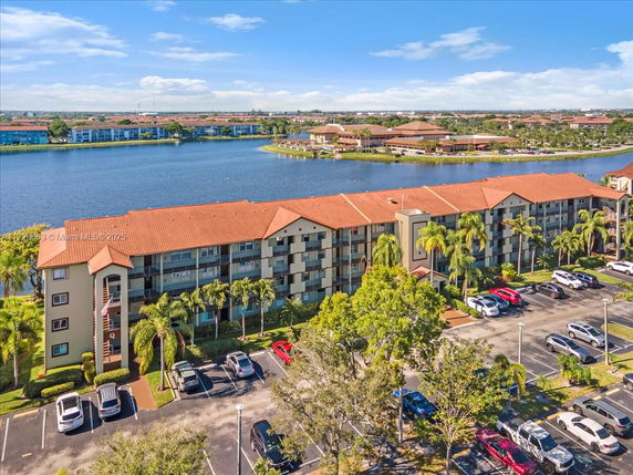 Aerial view of an apartment building with a parking lot and a lake in the background.