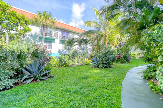 Front view of a multi-story building with balconies and surrounded by lush greenery.