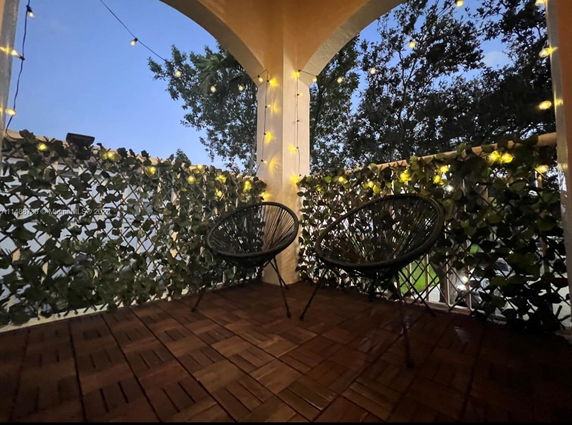 Decorated balcony with lights and chairs, offering a view of trees outside.