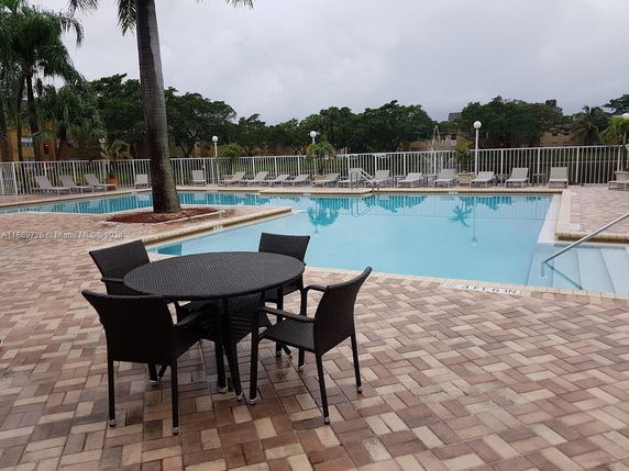 Outdoor swimming pool area with lounge chairs and a round table with chairs on a tiled deck.