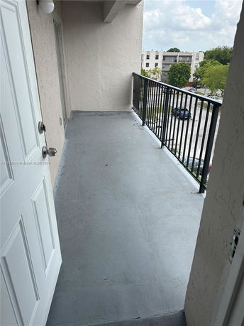 View from a balcony overlooking a residential area with parked cars and trees.