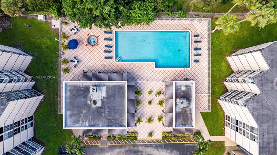 Aerial view of a swimming pool area surrounded by buildings with lounge chairs and umbrellas.