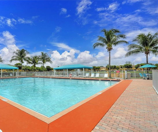 Outdoor swimming pool area with lounge chairs and palm trees.