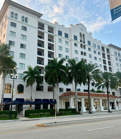Front view of a multi-story building with balconies and palm trees in front.
