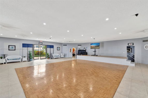 Spacious indoor recreational room with a wooden floor area, stage, seating, and a TV.