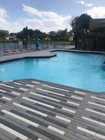 Pool area with lounge chairs and a fence, overlooking a body of water.