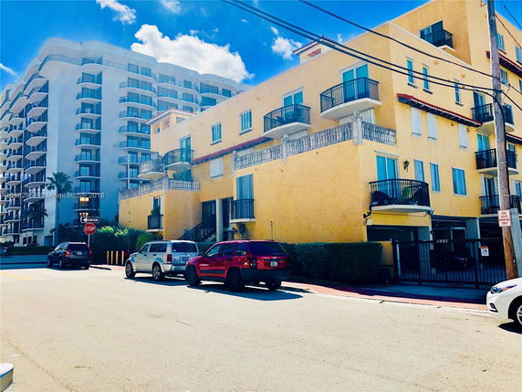 Front view of a multi-story yellow building with balconies, situated next to another taller building.
