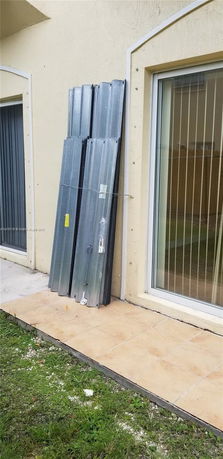 Exterior view of a house with sliding glass door and metal panels stored against the wall.