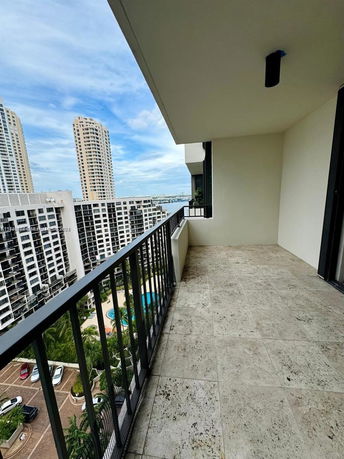 Balcony view overlooking high-rise buildings and a pool area below.