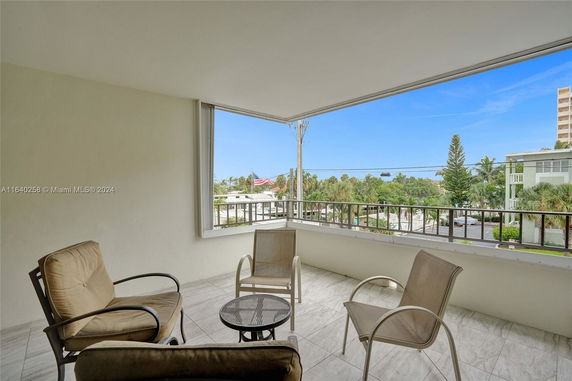 Panoramic view from a balcony with chairs and a small table overlooking surrounding greenery and buildings.