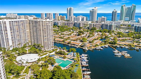 Aerial view of a waterfront cityscape with tall apartment buildings, a marina, and residential areas.