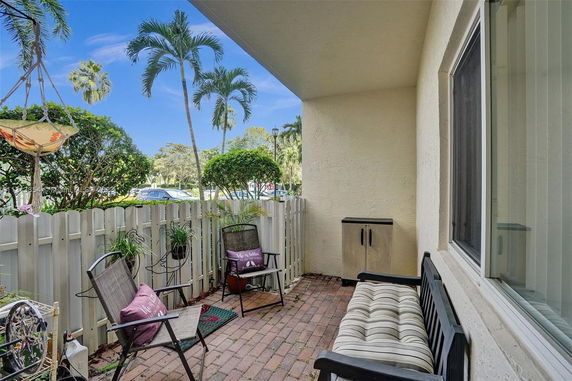 Outdoor patio area with seating and view of palm trees and a fenced yard.