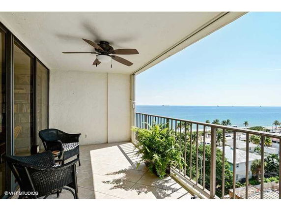 Balcony view overlooking the ocean with a ceiling fan, chairs, and a potted plant.