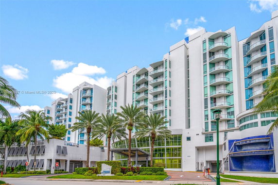 Front view of a modern multi-story apartment building with balconies and palm trees.