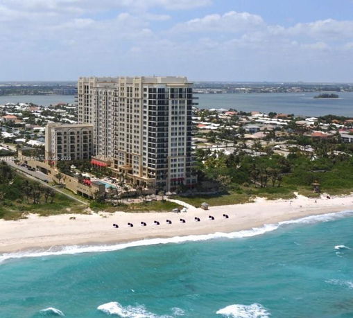 Aerial view of a large beachfront building with surrounding residential area and water body.