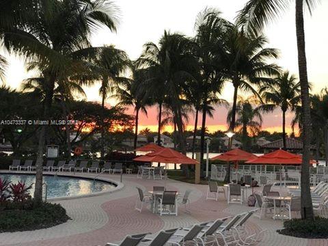View of a poolside area with lounge chairs and umbrellas, surrounded by palm trees at sunset.
