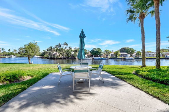 Wide-angle view of a patio with outdoor furniture overlooking a waterway and houses on the opposite bank.