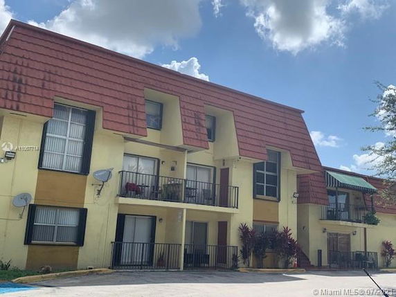Front view of a multi-story apartment building with balconies and red tiled roof elements.