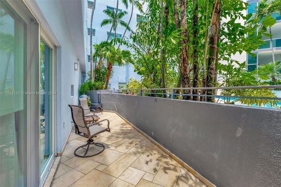 Outdoor patio area with chairs, plants, and railing adjacent to a building.