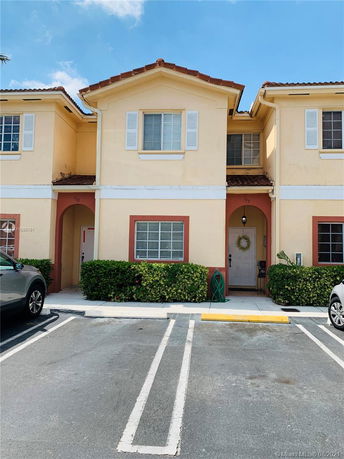 Front view of a two-story townhouse with beige walls and a red-tiled roof.