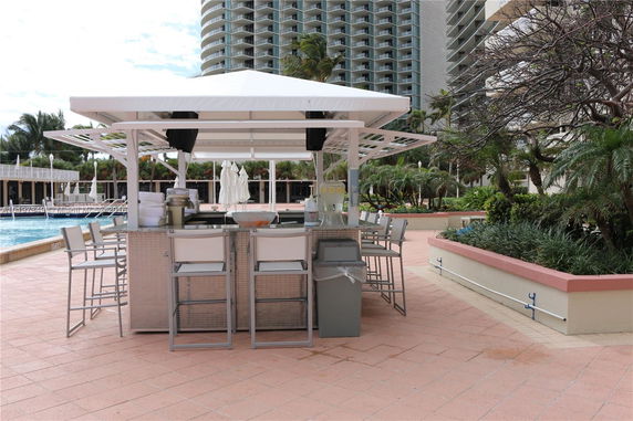 Outdoor seating area with bar stools and canopy near a swimming pool in an apartment complex.