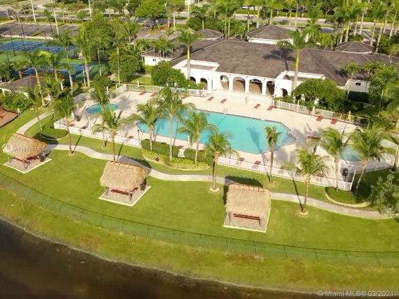 Aerial view of a swimming pool area with a clubhouse surrounded by palm trees and cabanas.