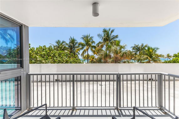 Balcony view with palm trees and ocean in the background.